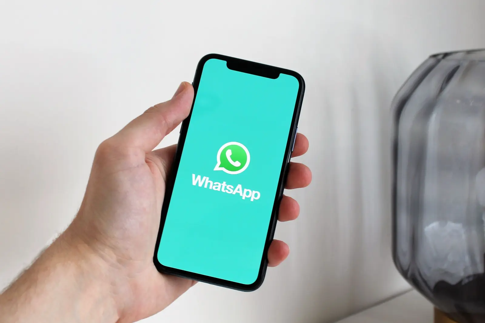 יד אוחזת בטלפון שעל המסך שלו מופיע הלוגו של WhatsApp.